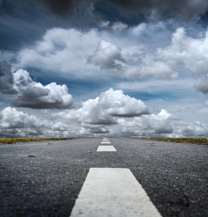 A straight road stretched toward a dramatic sky filled with fluffy clouds, creating a sense of journey.
